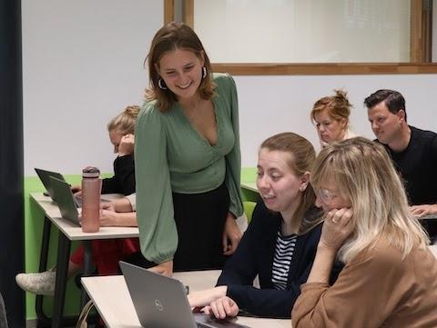 AI trainer geeft een deelnemer persoonlijke begeleiding achter de laptop tijdens een praktische cursus.